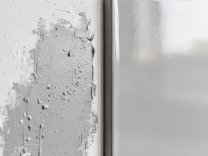 Malarz nakłada białą farbę wałkiem na ciemną, lakierowaną boazerię, odświeżając wnętrze salonu.